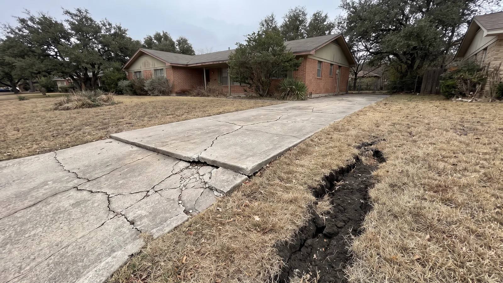 Old driveway cracked and heaved by expansive black clay soil in Central Texas